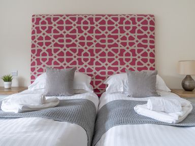 A bedroom with two single beds with grey cushions and white towels on grey throws at Hazelseat House in Graythwaite near Ulverston