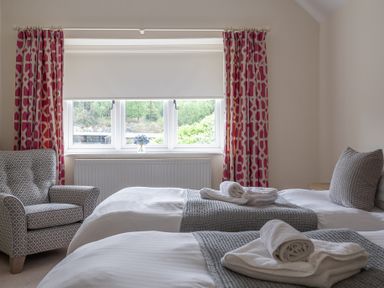 A bedroom with two single beds and a patterned armchair near a window with pink curtains at Hazelseat House in Graythwaite near Ulverston
