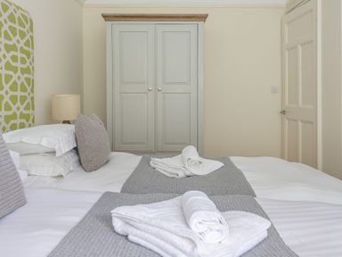 A bedroom with two beds side by side with grey bed runners and folded white towels a lamp beside one bed a wardrobe and a closed door at Hazelseat House in Graythwaite near Ulverston