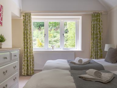 A bedroom with two single beds towels on beds a chest of drawers and a window with green patterned curtains at Hazelseat House Graythwaite near Ulverston