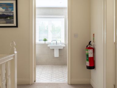 A hallway with a fire extinguisher on the wall and a bathroom with a sink and a plant on the windowsill at Hazelseat House in Graythwaite near Ulverston