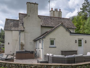 An outdoor patio area with garden furniture a hot tub and a stone wall at Hazelseat House in Graythwaite near Ulverston