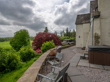 An outdoor patio with metal chairs and a hot tub near a cream-colored building at Hazelseat House Graythwaite near Ulverston