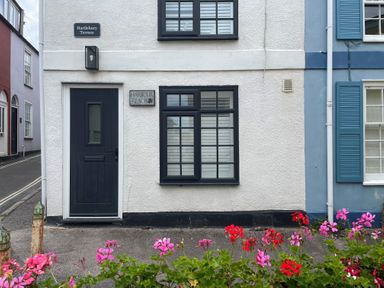 Front of a white building with a dark door and windows with a street sign Hartlebury Terrace and flowers in front at Harbour Reach Brewers Quay Harbour