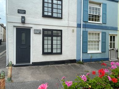 The exterior of houses with black and blue painted doors next to flowers at Harbour Reach in Brewers Quay Harbour