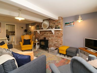 A living room with yellow and gray chairs a brick fireplace and a television at Harbour Reach Brewers Quay Harbour