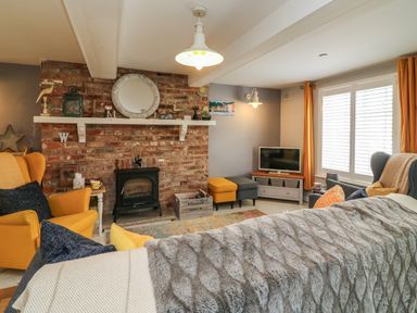 A living room with a brick fireplace yellow armchairs a television and a window with orange curtains at Harbour Reach Brewers Quay Harbour