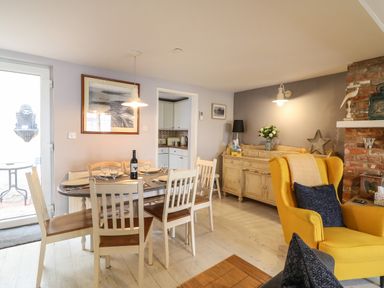 A dining area with a wooden table and six chairs a yellow armchair and a sideboard with a lamp and flowers at Harbour Reach Brewers Quay Harbour