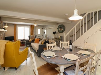 A dining area with a round table set with plates and glasses next to a living room with sofas and armchairs at Harbour Reach in Brewers Quay Harbour