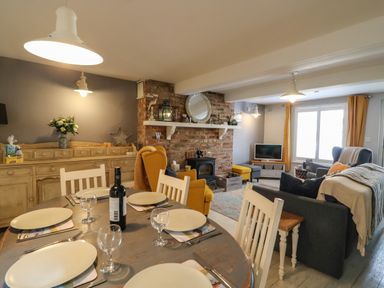 A dining area with a table set for six and a living room with chairs sofas and a brick fireplace at Harbour Reach in Brewers Quay Harbour