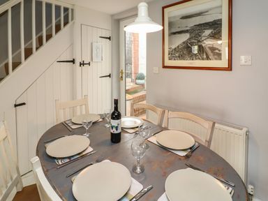 A dining room with a round table set with six plates and glasses and a bottle of wine with white chairs and a door under stairs at Harbour Reach in Brewers Quay Harbour