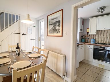 A dining area with a round table set with plates glasses and cutlery and a kitchen with white cabinets and tiled floor at Harbour Reach in Brewers Quay Harbour