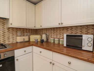 A kitchen corner with white cabinets a wooden countertop a microwave toaster kettle bread box three canisters and two mugs at Harbour Reach Brewers Quay Harbour
