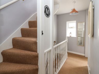 A staircase with brown carpet and white banisters leading to a hallway with a window mirror and hanging light at Harbour Reach in Brewers Quay Harbour