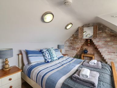 A bedroom with a striped blue bedspread two bedside tables with lamps and a brick wall with a small window at Harbour Reach Brewers Quay Harbour