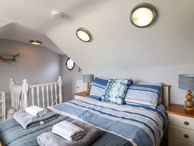 A bedroom with a bed with blue striped bedding two bedside tables with lamps and folded towels at Harbour Reach in Brewers Quay Harbour