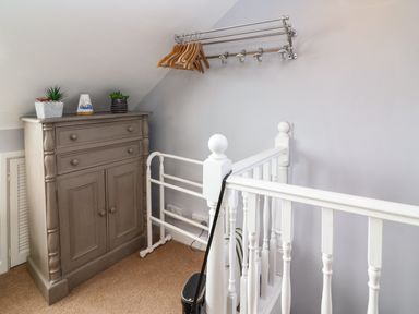A corner with a wooden cabinet with plants on top hangers on a metal rack and white wooden stair railing at Harbour Reach in Brewers Quay Harbour