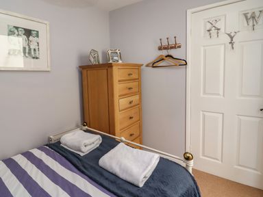 A bedroom with a bed with folded towels a wooden chest of drawers and a door with hooks at Harbour Reach Brewers Quay Harbour