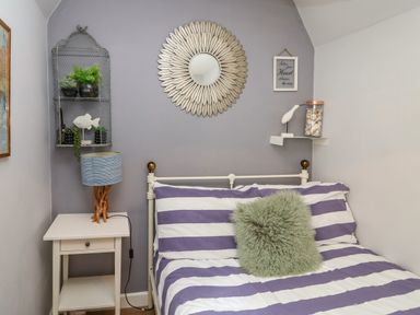 A bedroom with a striped bed, a green pillow, a nightstand with a lamp, wall shelves, and decorative items at Harbour Reach in Brewers Quay Harbour