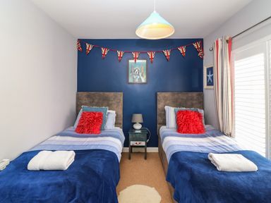 A bedroom with two single beds a blue accent wall and a nightstand with a lamp at Harbour Reach in Brewers Quay Harbour