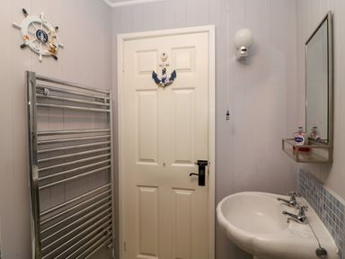 A bathroom with a white door featuring an anchor decoration a chrome towel warmer a white sink with dual taps and a mirror above at Harbour Reach Brewers Quay Harbour