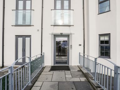 The entrance door of a modern apartment building with railings on both sides of the pathway at Steps Away Benllech