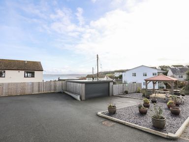 Outdoor area with a wooden fence garage and a gazebo with picnic tables and potted plants at Steps Away in Benllech