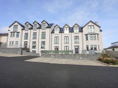 A large white residential building with multiple windows and balconies and a paved parking area in front at Steps Away in Benllech