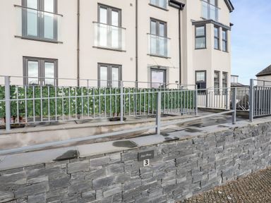 A building with grey framed windows and railings with a stone wall and a sign displaying number 3 at Steps Away in Benllech