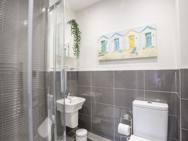 A bathroom with a shower enclosure a sink a toilet and a painting at Steps Away in Benllech