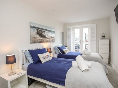 A bedroom with two single beds blue bedding a nightstand with a lamp and a painting of a boat at Steps Away in Benllech