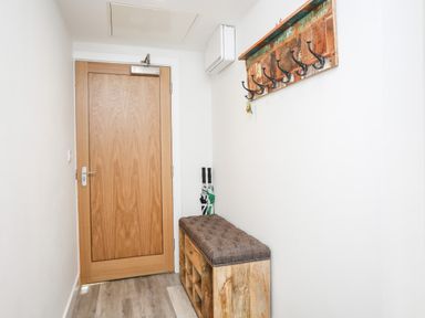 A hallway with a wooden door a wooden bench with cushions and a wall-mounted coat rack at Steps Away in Benllech