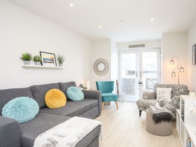 A living room with a gray sofa with cushions a teal chair a patterned armchair a round mirror and potted plants at Steps Away in Benllech