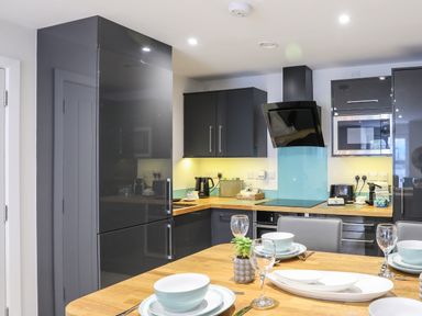 A kitchen with black cabinets appliances and a wooden dining table set with dishes at Steps Away in Benllech
