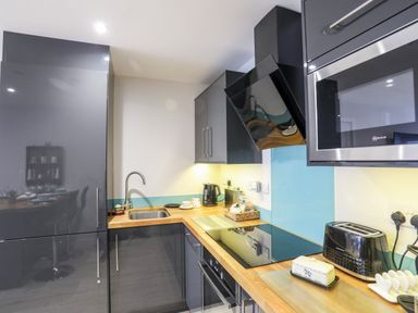 A kitchen with a sink an electric stove a microwave a toaster and cabinets at Steps Away in Benllech