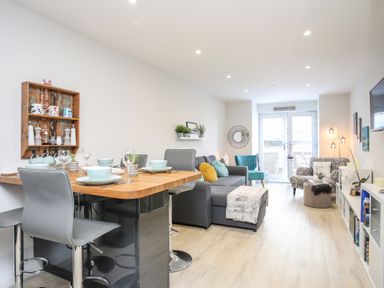 A living room and dining area with a wooden dining table set with dishes and glassware at Steps Away in Benllech