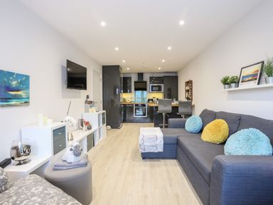 An open plan living room and kitchen with a gray sofa and colorful pillows at Steps Away in Benllech