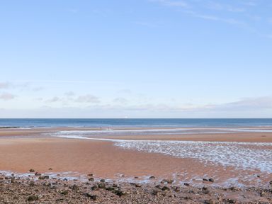 A beach with scattered rocks and pools of water near the shore at Steps Away in Benllech