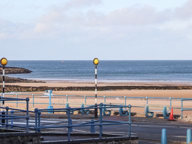 A view of a sandy beach and ocean with blue railings and road barriers in the foreground at Steps Away in Benllech