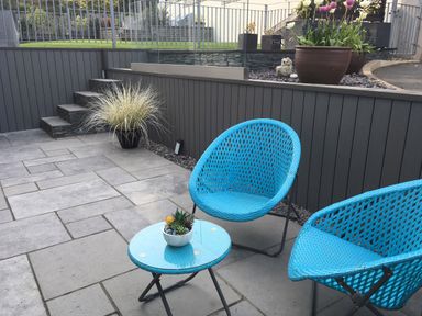 A patio area with two blue chairs and a small round table with a potted plant at Steps Away in Benllech