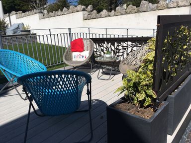 An outdoor patio with blue and beige wicker chairs a small round table with a potted plant and large planter boxes with plants at Steps Away in Benllech