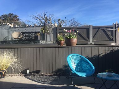 An outdoor patio area with a blue chair, a small table, potted plants, and a gray fence at Steps Away in Benllech