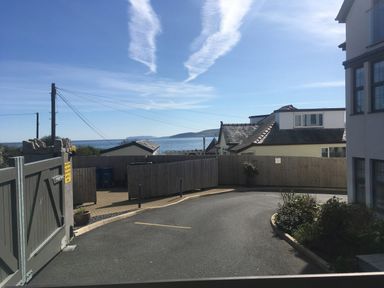A paved driveway with a gate and fenced yard overlooking houses and a distant sea at Steps Away in Benllech