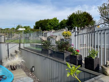 An outdoor patio area with potted plants chairs and a metal fence at Steps Away in Benllech