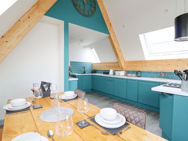 A kitchen with teal cabinets wooden beams and a dining table with place settings at Kerry Hill - The Sheepfold in Llanyre near Llandrindod Wells