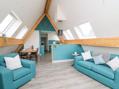 An attic living area with turquoise sofas dining table and kitchen at Kerry Hill - The Sheepfold in Llanyre near Llandrindod Wells