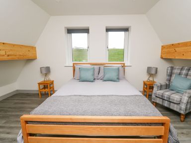 A bedroom with a wooden bed and two windows with nightstands and lamps and a plaid armchair at Kerry Hill - The Sheepfold in Llanyre near Llandrindod Wells