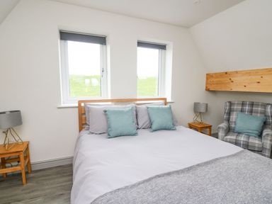 A bedroom with a double bed, two windows, two bedside tables with lamps, and a plaid armchair at Kerry Hill - The Sheepfold in Llanyre near Llandrindod Wells
