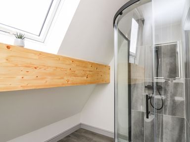 A bathroom with a glass shower enclosure a skylight window a wooden beam and a small plant on the beam at Kerry Hill - The Sheepfold in Llanyre near Llandrindod Wells