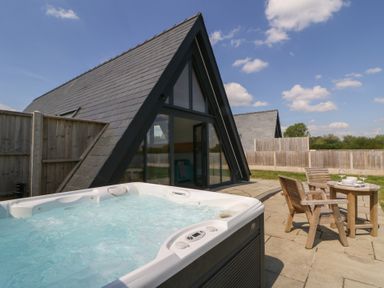 A patio with a hot tub and wooden chairs with a table outside a triangular roof building at Kerry Hill - The Sheepfold in Llanyre near Llandrindod Wells